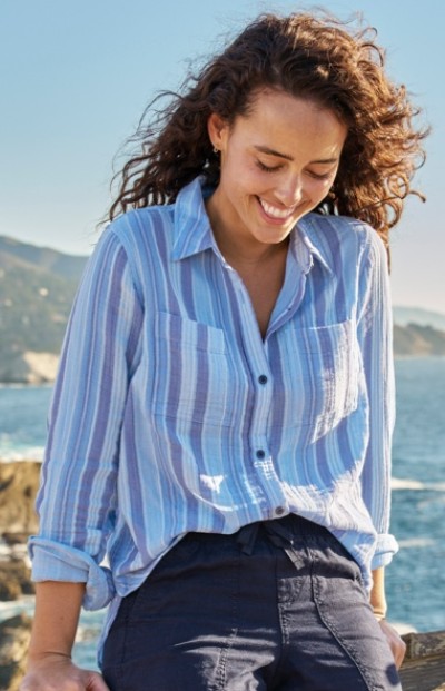 A woman with curly hair wearing a blue and white striped shirt, standing outdoors near a body of water.