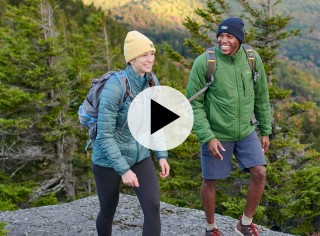 2 people hiking, a play video icon in the center.