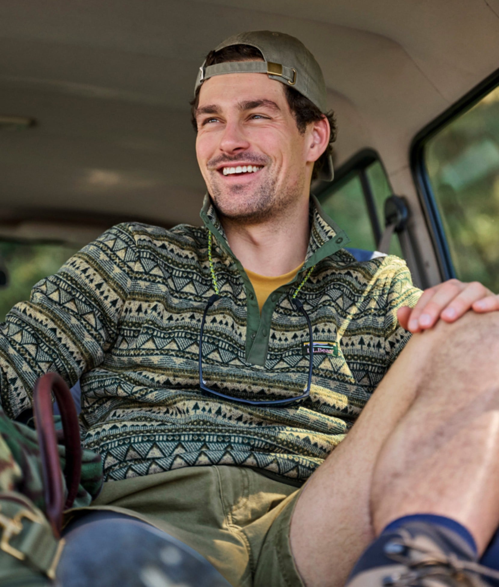 Man sitting in a vehicle wearing a patterned fleece pullover and cap. 