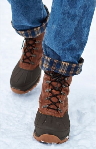 A person wearing flannel lined jeans and storm chaser boots walks on the snow.