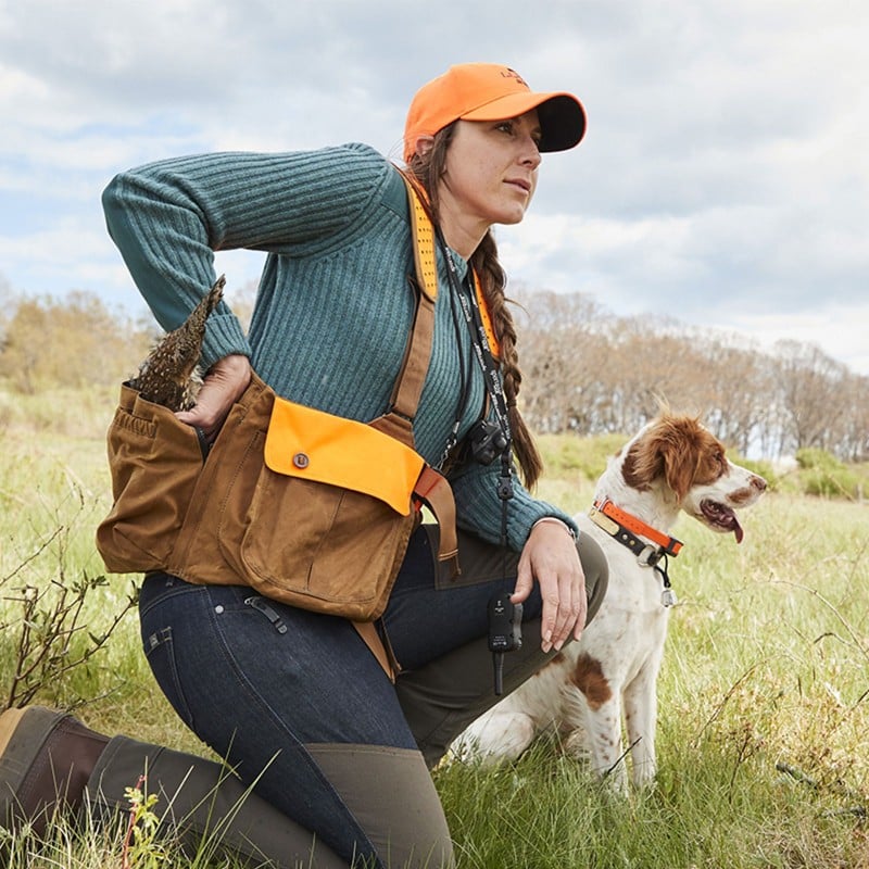 A dog sitting between two hunters looking intently into the distance.