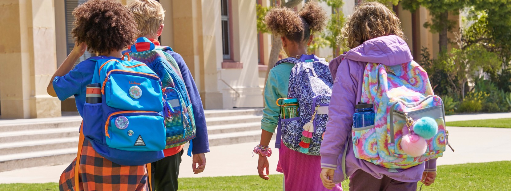 4 kids walking toward their school wearing school backpacks.