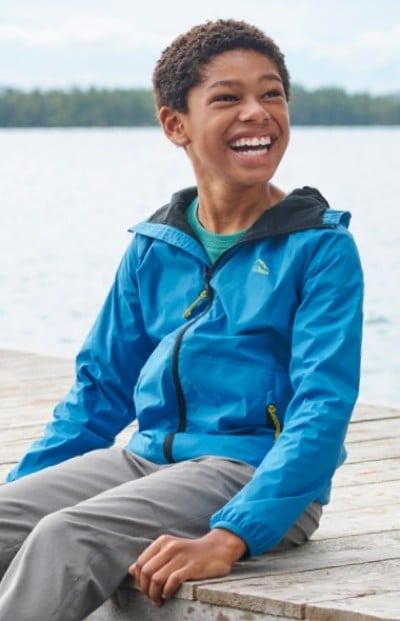 Boy sitting on wooden dock wearing blue rain jacket