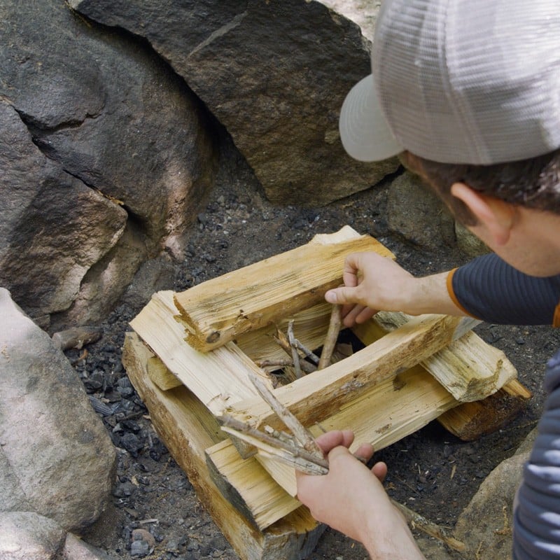 Nate placing a fuel log on either side of a pile of tinder.