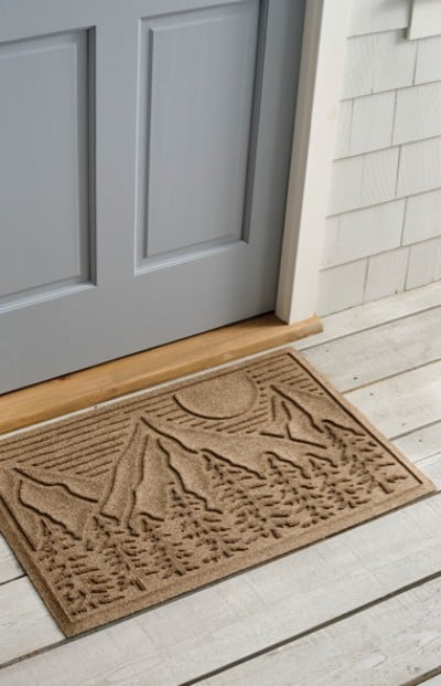 A L L Bean doormat with a mountainous landscape design is placed in front of a grey door on a wooden floor