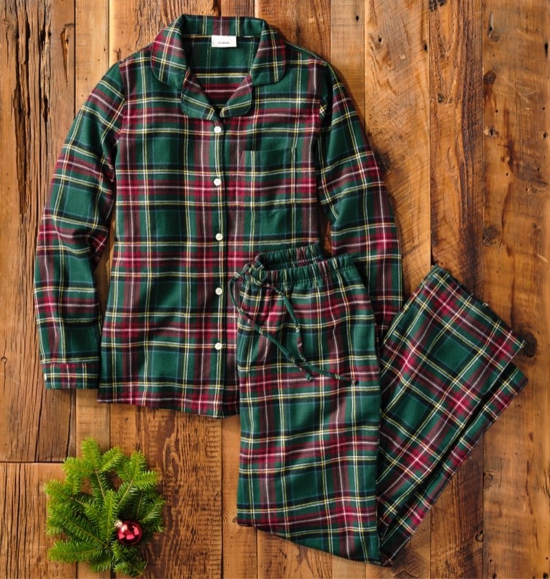 Plaid pajama set laid out on a wooden floor with a pine branch.
