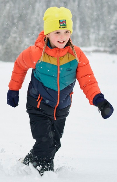 A child in colorful L L Bean winter gear walks in snow; a moment of childhood joy and winter’s essence captured. 