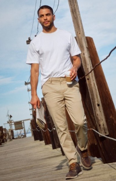 Person walking on a dock carrying a coffee cup while wearing a white T-shirt and khaki pants.
