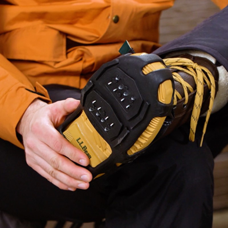 Close-up of a seated person with one foot on their knee, showing the traction device on the bottom of their boot.