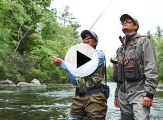 A man and woman in waders fly-fishing in a river.