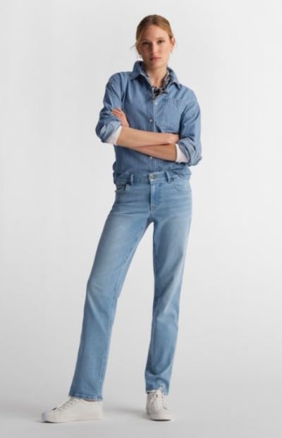 Person in a denim shirt and jeans standing in a studio with arms crossed.