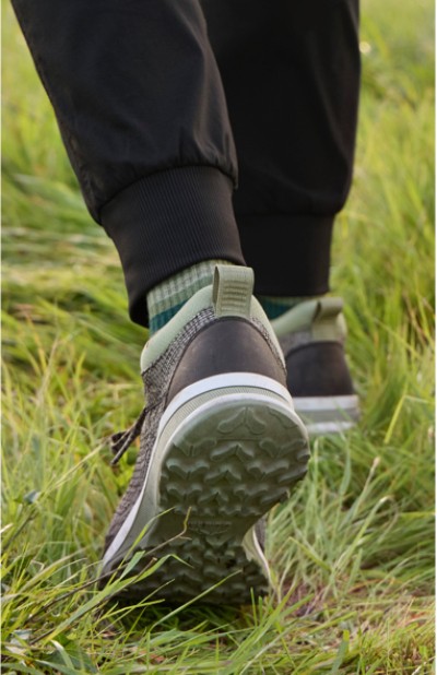 A close up of a person wearing L L Bean walking in grass, highlighting the details of the shoes and the natural setting.