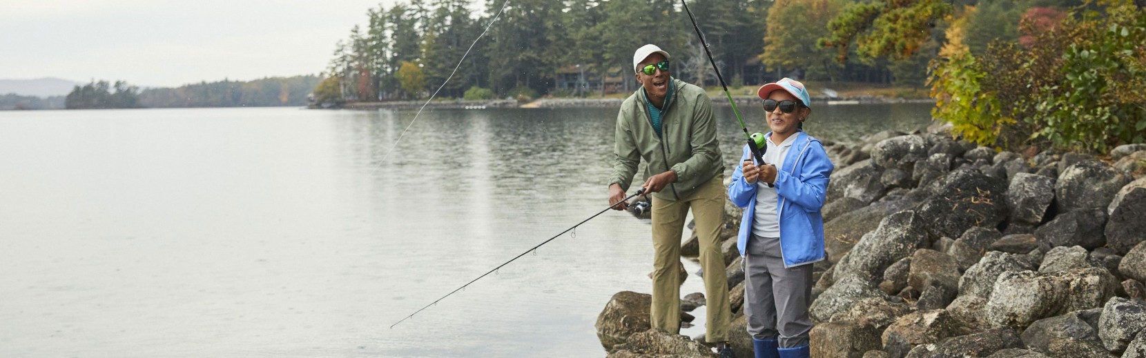 A child and man fishing on a rocky shore.