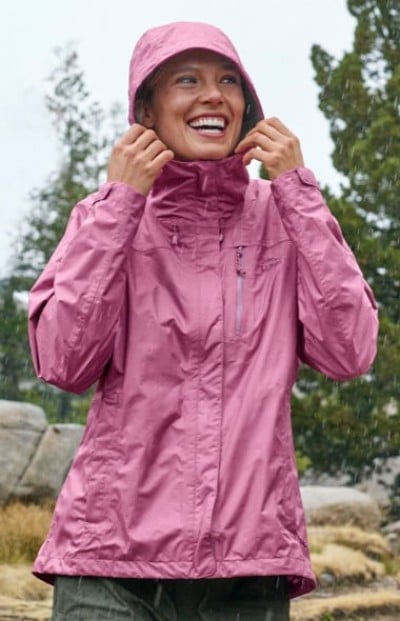 Person in pink hooded rain jacket with zippered chest pocket, designed for wet weather outdoor activities.