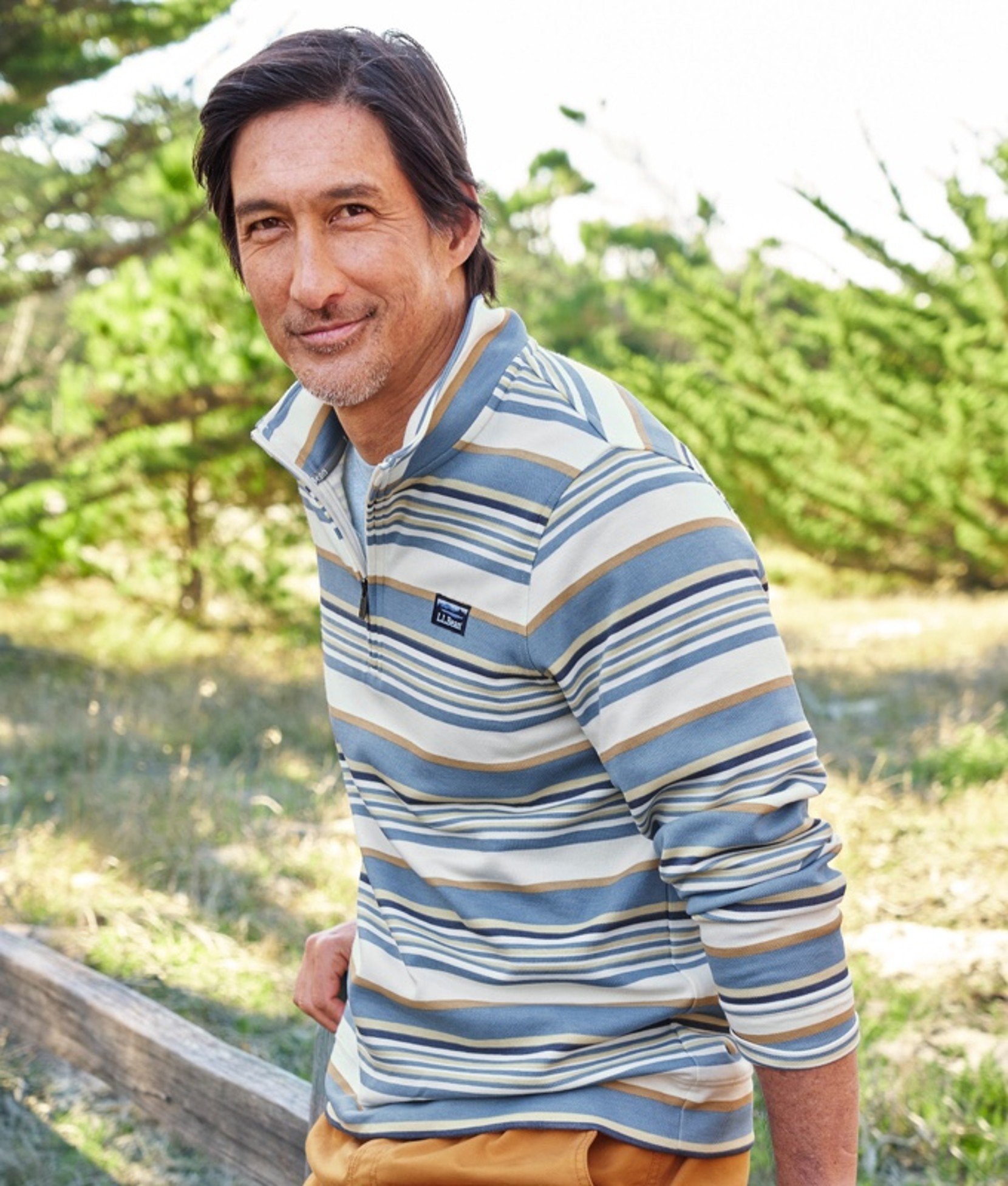 Waist up shot of a man outside leaning on a fence.