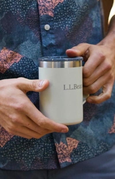 A person wearing a patterned shirt holds a white L L Bean mug with both hands.