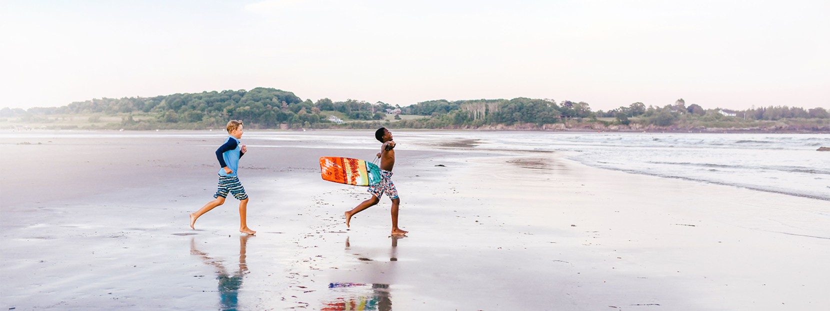 Children with a body board running on the beach.