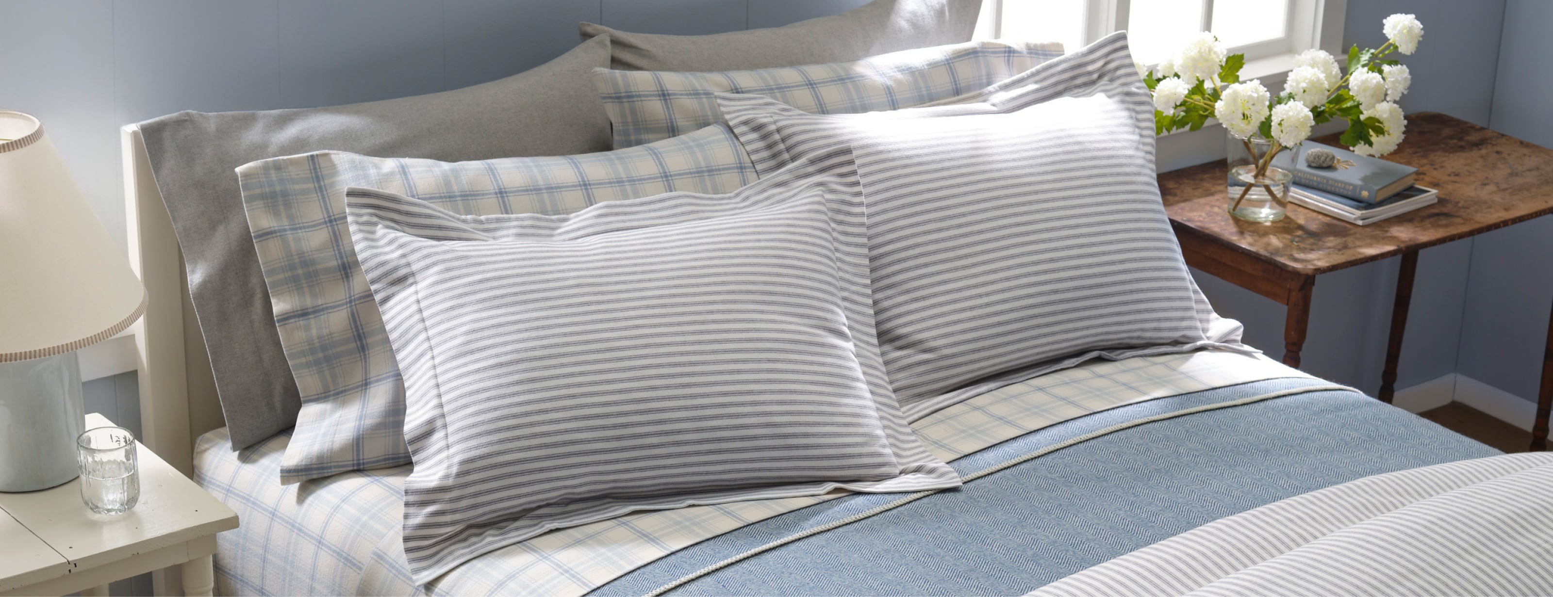 Neatly made bed with patterned blue and white pillows, blankets and bedding in a cozy room.