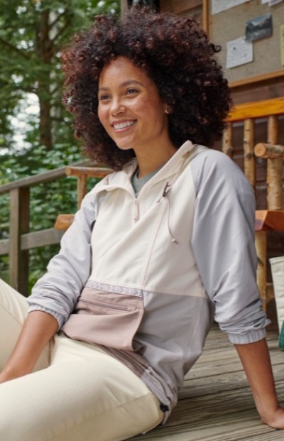A woman with curly hair sits on wooden steps outdoors, wearing a light gray and white jacket.