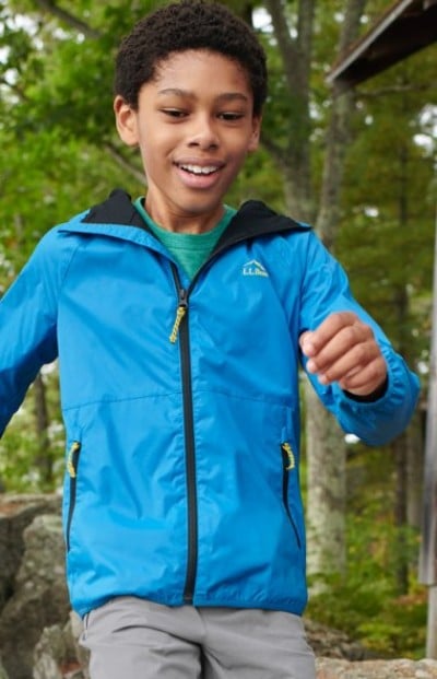 Achild in a blue rain jacket outdoors in a forested area.