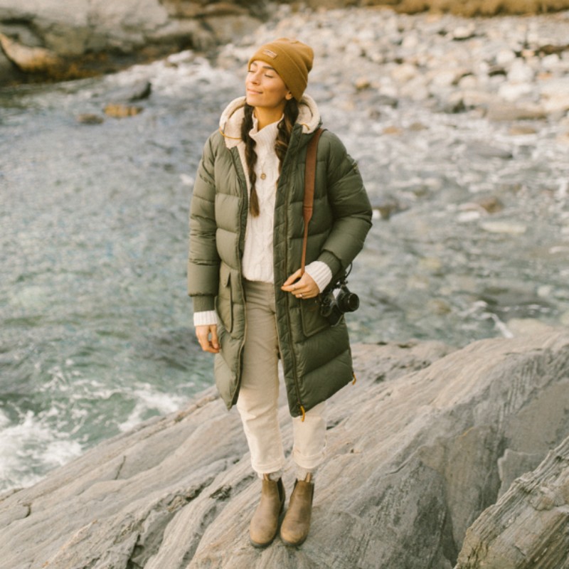 A woman standing on a rock at the ocean's edge, face tipped to the sun.