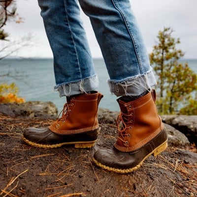 Person in brown L L Bean boots and rolled-up jeans by a lake.