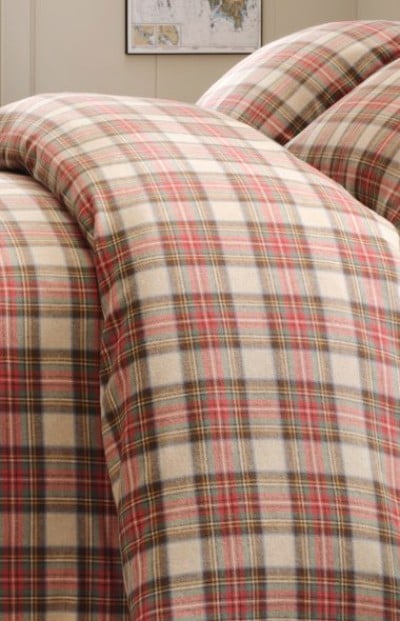 A cozy bed made with beige and red plaid bedding, creating a warm and inviting layered look.