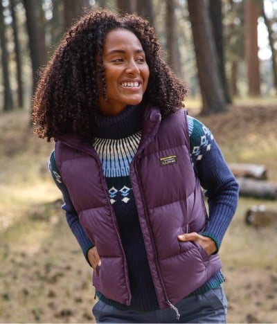 Woman in purple vest and patterned sweater standing in a forest.