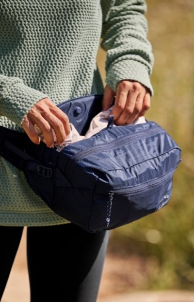 Close up of hands packing a navy zippered waist pack outdoors while wearing a knit sweater.