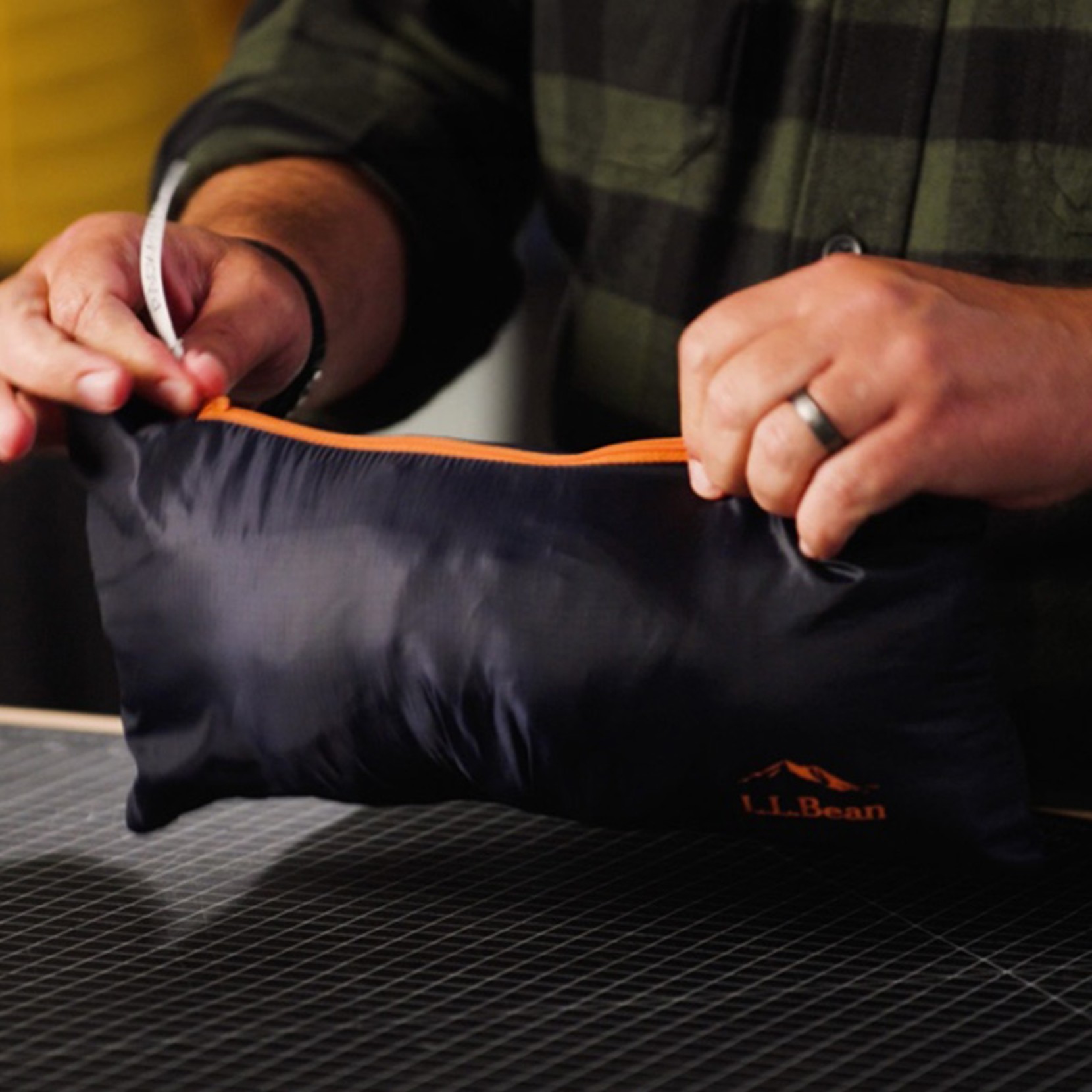 Hands holding packed black L.L.Bean jacket in orange-trimmed pouch.