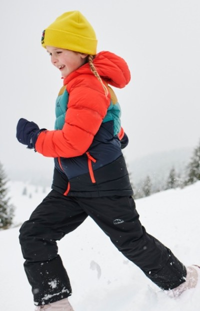 Child outside wearing snow pants, jacket and hat running through snow.