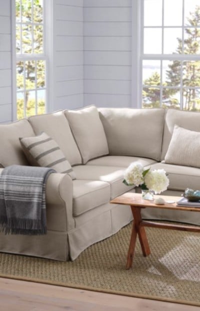 Beige sectional sofa with striped and solid pillows sits in a bright room, accented by a gray throw and wooden coffee table.
