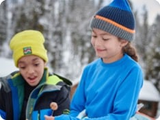 A boy and girl in L.L.Bean outerwear and base layers sitting by a campfire.