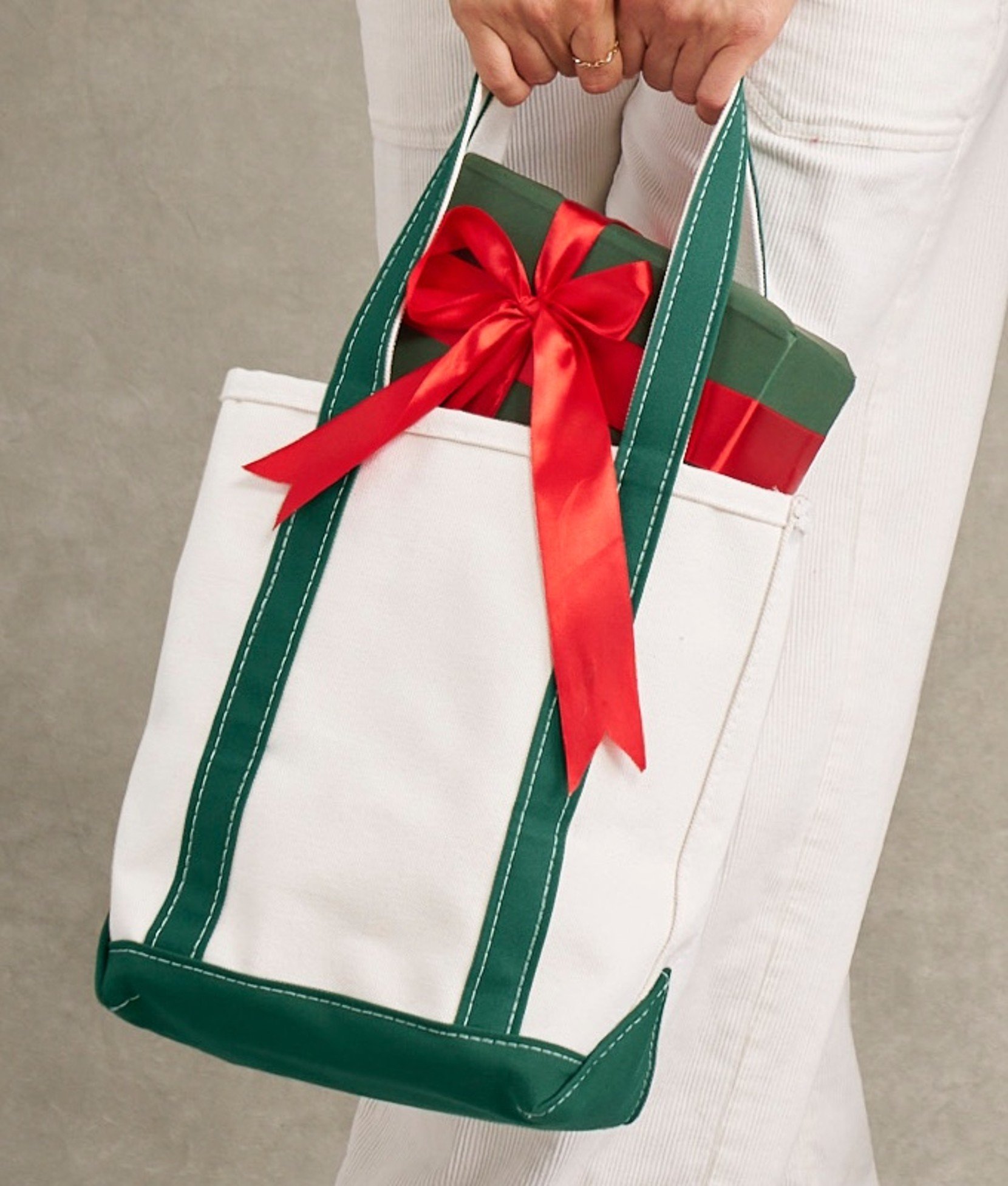 White tote bag with green trim and red ribbon handles. 