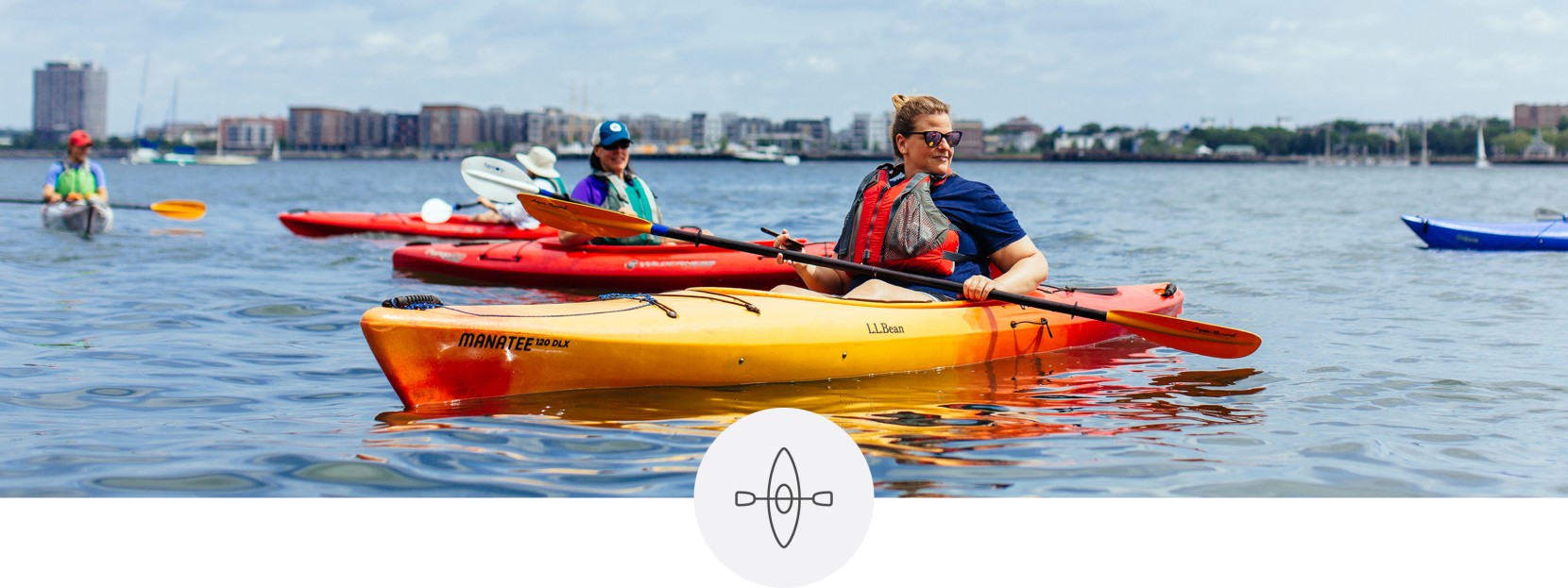 Several kayakers on the water, a cityscape in the background.