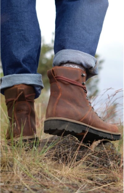 A close up of a person’s lower legs wearing brown boots and blue jeans against a natural backdrop, capturing a moment of outdoor adventure.