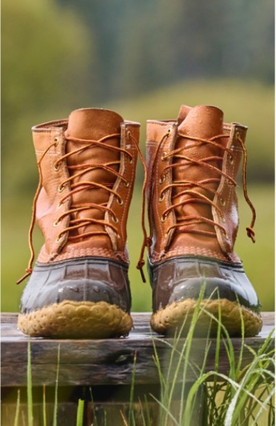 Brown leather lace-up L. L. Bean boots sit on a wooden surface outdoors, surrounded by green grass.