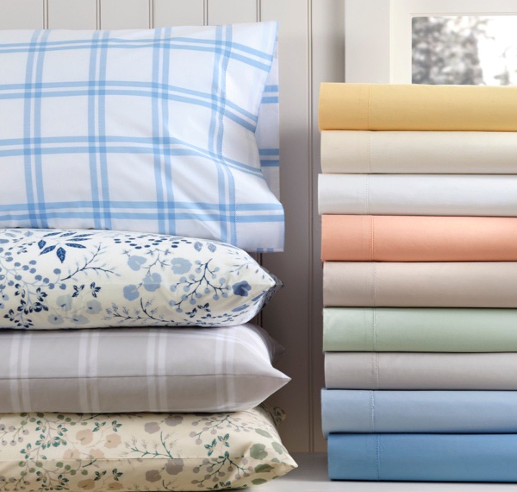 Stack of pastel percale sheets and patterned pillows arranged neatly. 