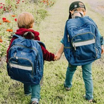 Two children wearing their bookpacks while holding hands
