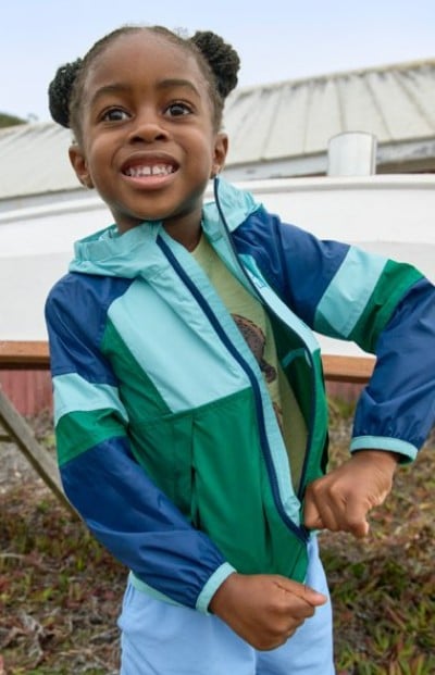 Child zipping up their green and blue jacket while standing outdoors.
