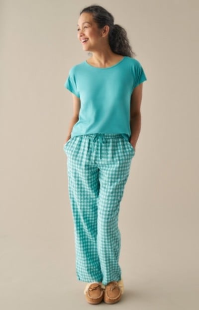 A woman wearing a teal t shirt, teal and white checkered pants, and brown moccasin slippers.