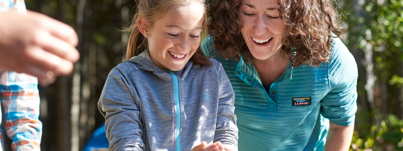 A smiling mother and daughter outside looking at something in the daughter's hands.