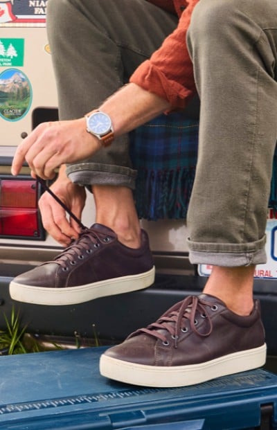 A person ties their shoe on a car bumper. 