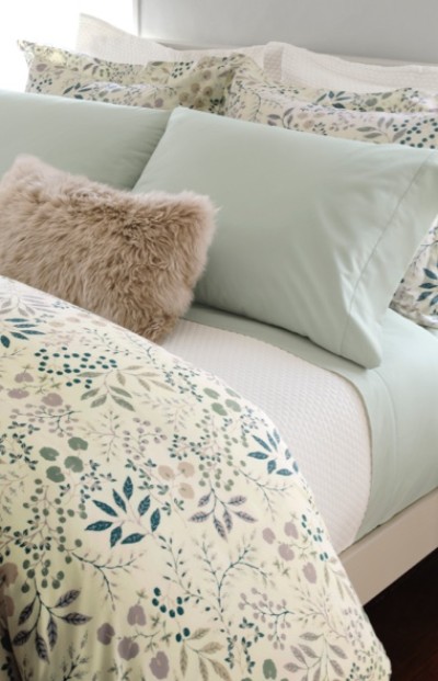 Bed with floral sheets, light green pillowcases, and a fluffy beige pillow; creating a soft and cozy appearance.