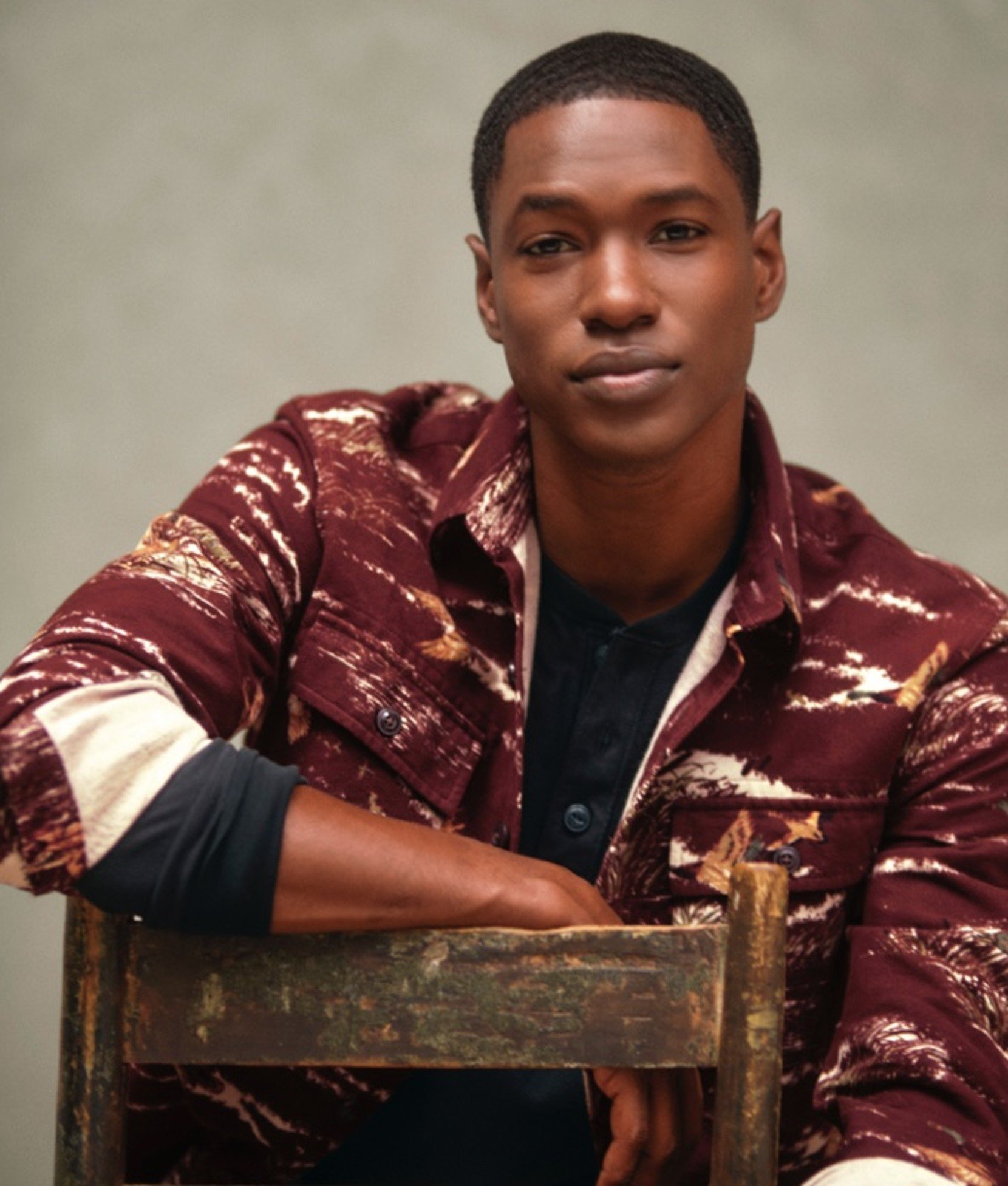Man in maroon and white patterned cardigan leaning on a chair. 