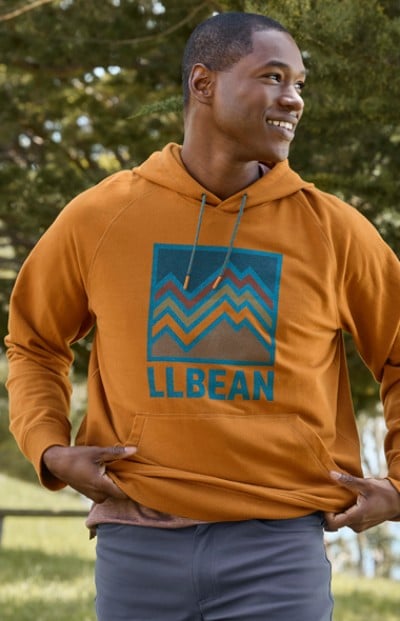 A man stands outdoors wearing an orange hoodie with an L L Bean logo.