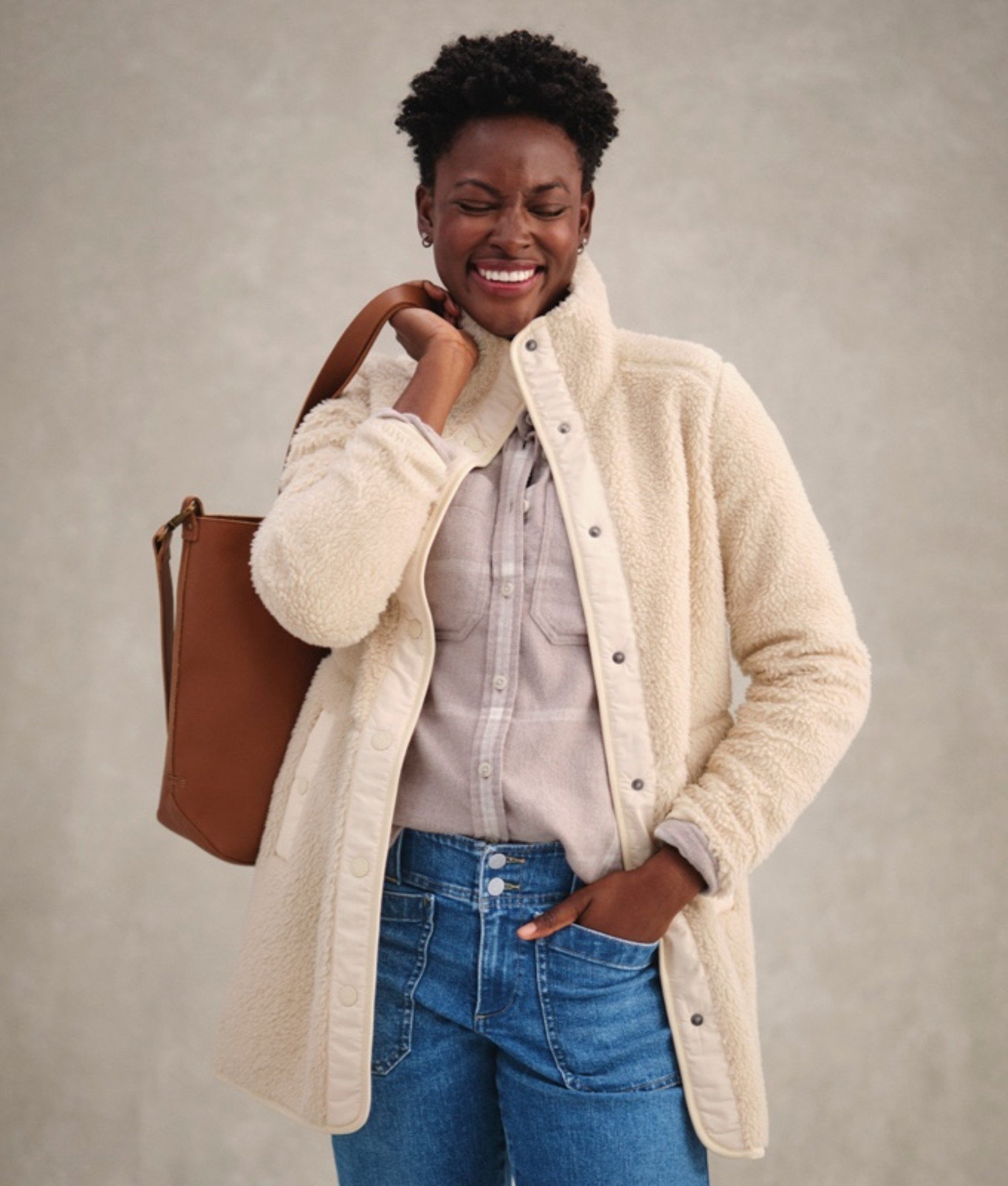 Woman in beige coat holding a brown handbag over her shoulder. 