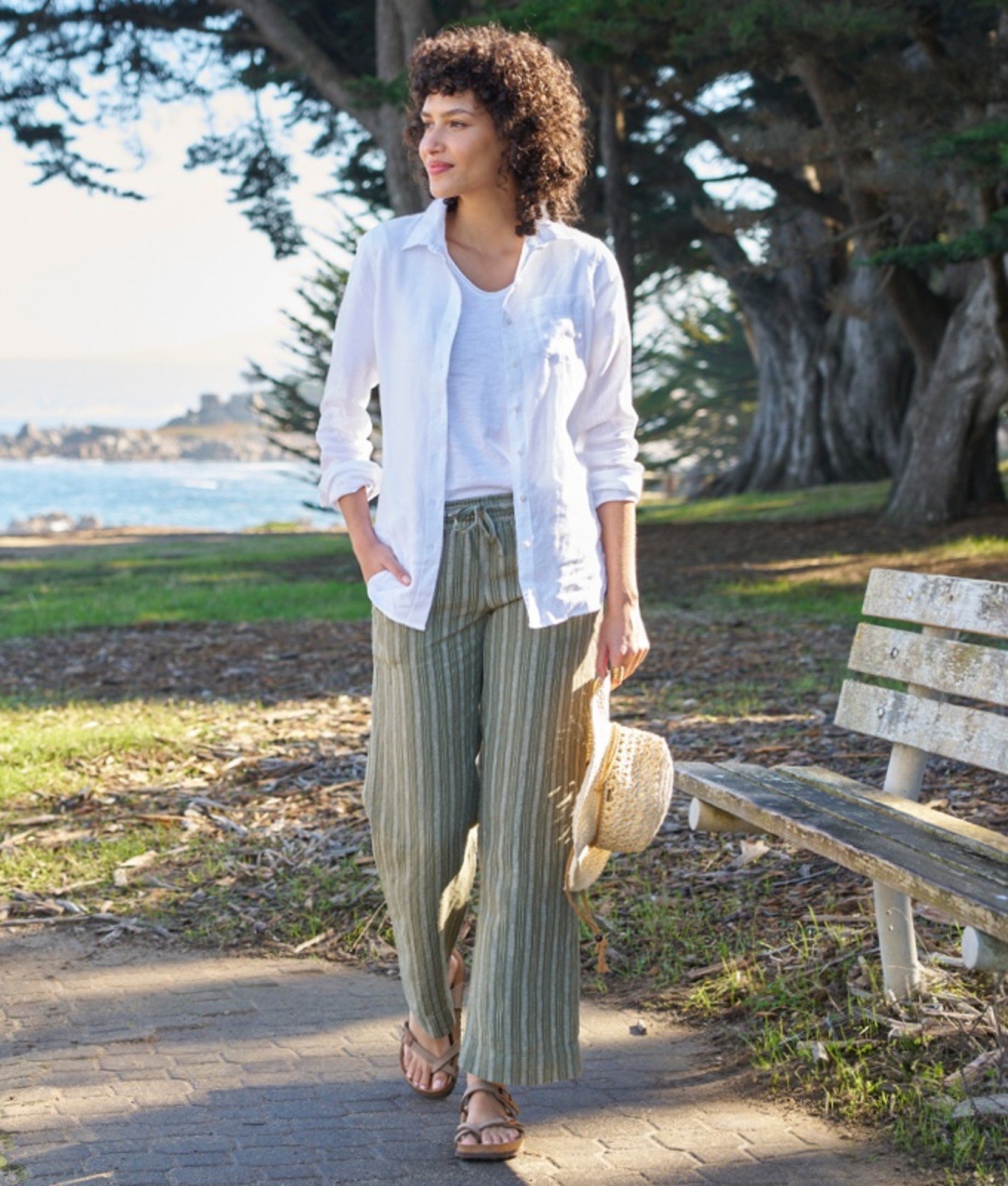 A woman walking outside on a path passing a park bench.
