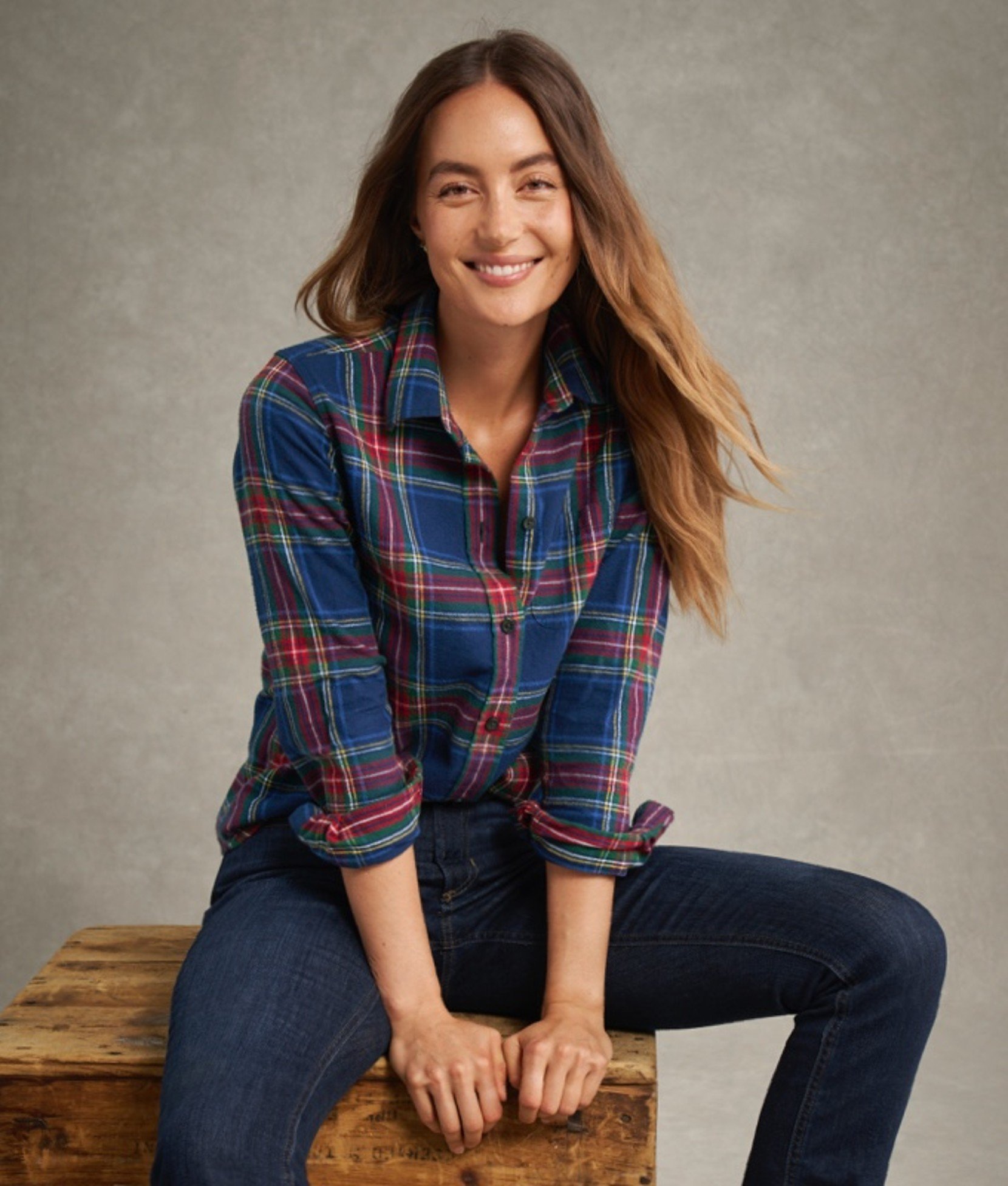Woman in blue and red plaid flannel shirt sitting on a stool.