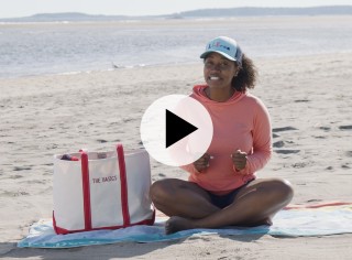 Stephanie sitting on a beach blanket at the beach, a play video icon in the center.